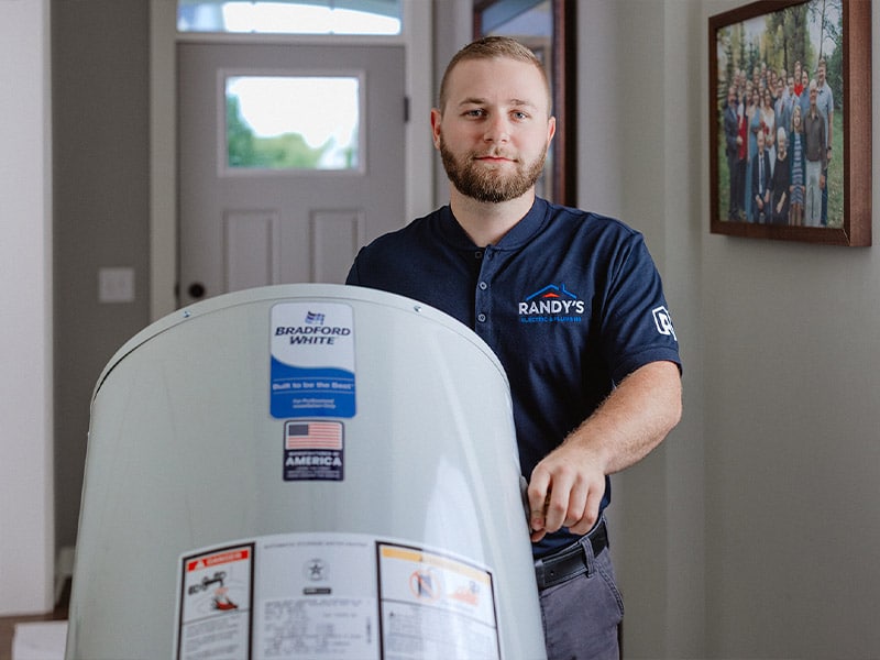 A man in a Randy's shirt with a Bradford White water heater inside a house.